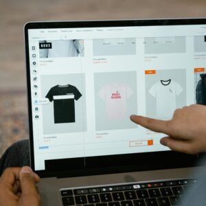A person points to t-shirt options in an online store on a laptop screen.